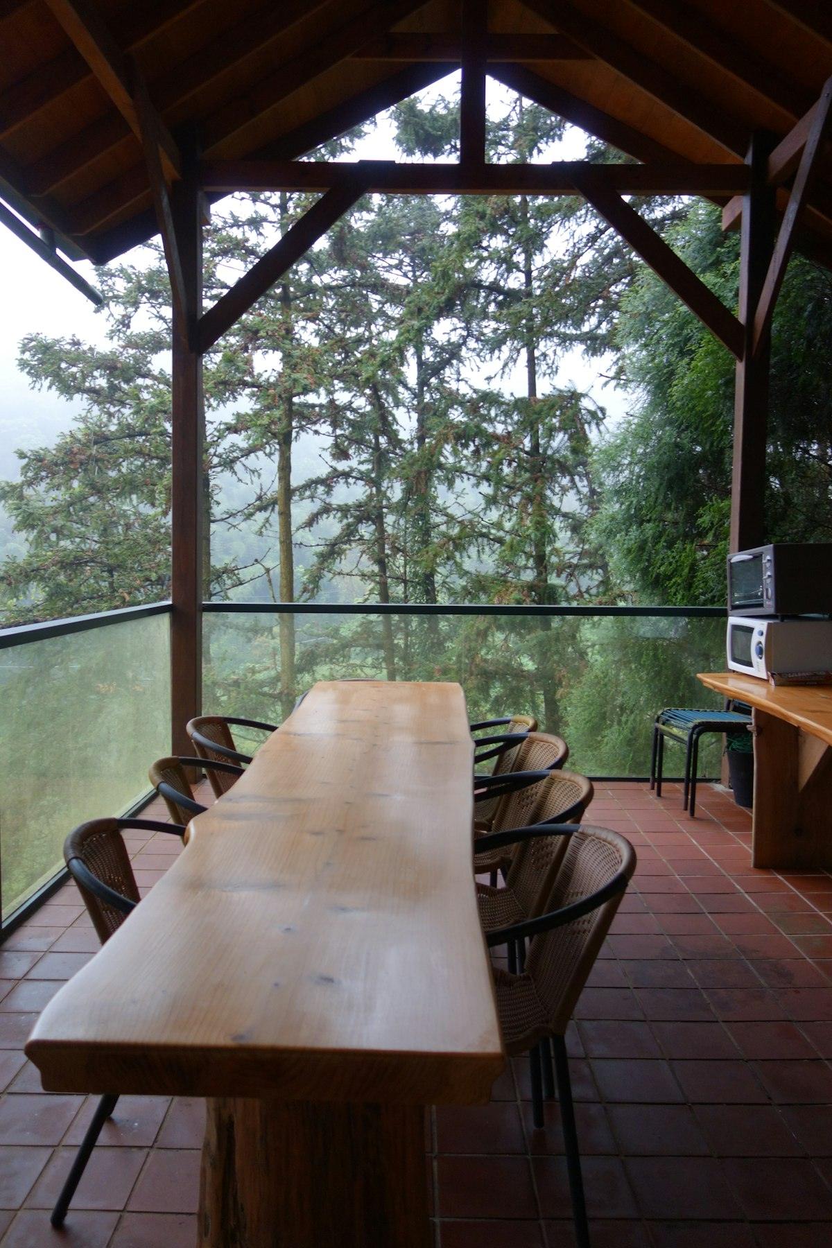 The south terrace in the morning: a wooden table and chairs under the eaves, green hills beyond